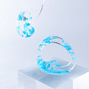 使用限界を超え廃棄されるカプセルトイのカプセルから生まれたオリジナルのアクセサリー「mom（マム）」です。 有限会社三幸の装飾アクリル板製造技術によって作られた、浮遊感のある水中のような表情が美しいアクリル素材を使用。 ミニチュアが入っていたカプセルからインスピレーションを受け、豆型のピースが包み込まれるようにデザインされたイヤーアクセサリーです。 イアーカフとピアス（イアリング）をセパレートで使用できます。KiNaKoとのコラボレーションによって生まれました。 デザイン/KiNaKo