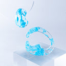 使用限界を超え廃棄されるカプセルトイのカプセルから生まれたオリジナルのアクセサリー「mom（マム）」です。 有限会社三幸の装飾アクリル板製造技術によって作られた、浮遊感のある水中のような表情が美しいアクリル素材を使用。 ミニチュアが入っていたカプセルからインスピレーションを受け、豆型のピースが包み込まれるようにデザインされたイヤーアクセサリーです。 イアーカフとピアス（イアリング）をセパレートで使用できます。KiNaKoとのコラボレーションによって生まれました。 デザイン/KiNaKo