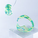 使用限界を超え廃棄されるカプセルトイのカプセルから生まれたオリジナルのアクセサリー「mom（マム）」です。 有限会社三幸の装飾アクリル板製造技術によって作られた、浮遊感のある水中のような表情が美しいアクリル素材を使用。 ミニチュアが入っていたカプセルからインスピレーションを受け、豆型のピースが包み込まれるようにデザインされたイヤーアクセサリーです。 イアーカフとピアス（イアリング）をセパレートで使用できます。KiNaKoとのコラボレーションによって生まれました。 デザイン/KiNaKo