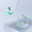 使用限界を超え廃棄されるカプセルトイのカプセルから生まれたオリジナルのアクセサリー「mom（マム）」です。 有限会社三幸の装飾アクリル板製造技術によって作られた、浮遊感のある水中のような表情が美しいアクリル素材を使用。 ミニチュアが入っていたカプセルからインスピレーションを受け、豆型のピースが包み込まれるようにデザインされたイヤーアクセサリーです。 イアーカフとピアス（イアリング）をセパレートで使用できます。KiNaKoとのコラボレーションによって生まれました。 デザイン/KiNaKo 