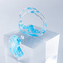 使用限界を超え廃棄されるカプセルトイのカプセルから生まれたオリジナルのアクセサリー「mom（マム）」です。 有限会社三幸の装飾アクリル板製造技術によって作られた、浮遊感のある水中のような表情が美しいアクリル素材を使用。 ミニチュアが入っていたカプセルからインスピレーションを受け、豆型のピースが包み込まれるようにデザインされたイヤーアクセサリーです。 イアーカフとピアス（イアリング）をセパレートで使用できます。KiNaKoとのコラボレーションによって生まれました。 デザイン/KiNaKo 