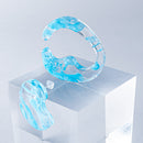 使用限界を超え廃棄されるカプセルトイのカプセルから生まれたオリジナルのアクセサリー「mom（マム）」です。 有限会社三幸の装飾アクリル板製造技術によって作られた、浮遊感のある水中のような表情が美しいアクリル素材を使用。 ミニチュアが入っていたカプセルからインスピレーションを受け、豆型のピースが包み込まれるようにデザインされたイヤーアクセサリーです。 イアーカフとピアス（イアリング）をセパレートで使用できます。KiNaKoとのコラボレーションによって生まれました。 デザイン/KiNaKo 