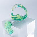 使用限界を超え廃棄されるカプセルトイのカプセルから生まれたオリジナルのアクセサリー「mom（マム）」です。 有限会社三幸の装飾アクリル板製造技術によって作られた、浮遊感のある水中のような表情が美しいアクリル素材を使用。 ミニチュアが入っていたカプセルからインスピレーションを受け、豆型のピースが包み込まれるようにデザインされたイヤーアクセサリーです。 イアーカフとピアス（イアリング）をセパレートで使用できます。KiNaKoとのコラボレーションによって生まれました。 デザイン/KiNaKo 