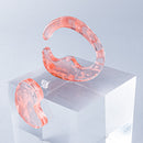 使用限界を超え廃棄されるカプセルトイのカプセルから生まれたオリジナルのアクセサリー「mom（マム）」です。 有限会社三幸の装飾アクリル板製造技術によって作られた、浮遊感のある水中のような表情が美しいアクリル素材を使用。 ミニチュアが入っていたカプセルからインスピレーションを受け、豆型のピースが包み込まれるようにデザインされたイヤーアクセサリーです。 イアーカフとピアス（イアリング）をセパレートで使用できます。KiNaKoとのコラボレーションによって生まれました。 デザイン/KiNaKo 