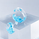 使用限界を超え廃棄されるカプセルトイのカプセルから生まれたオリジナルのアクセサリー「mom（マム）」です。 有限会社三幸の装飾アクリル板製造技術によって作られた、浮遊感のある水中のような表情が美しいアクリル素材を使用。 ミニチュアが入っていたカプセルからインスピレーションを受け、豆型のピースが包み込まれるようにデザインされたイヤーアクセサリーです。 イアーカフとピアス（イアリング）をセパレートで使用できます。KiNaKoとのコラボレーションによって生まれました。 デザイン/KiNaKo 